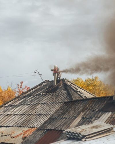 Chimney sweep cleaning a chimney standing balanced on the apex of a house roof lowering equipment down the flue