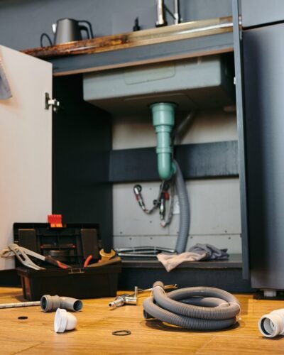 Open door of cabinet under sink in the kitchen, toolbox and plumbing equipment