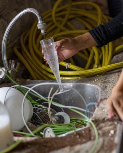 Person filling a glass with water at a cluttered sink.