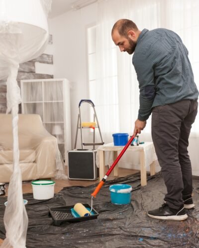 Man dipping the roller in blue paint during home development. Home during renovation, decoration and painting. Interior apartment improvement maintenance. Roller, ladder for house repair